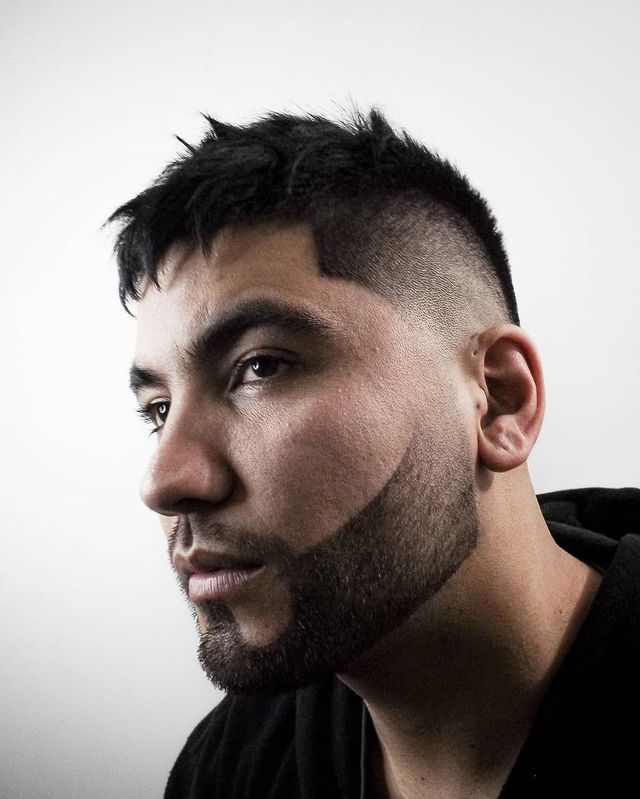 Fade haircut with sharp hair part and full beard, front angle