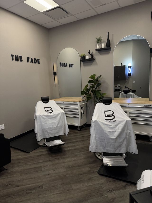 Two empty barber chairs with arched mirrors and blonde wood stations